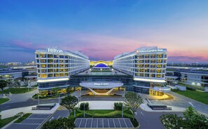 A modern hotel with a central atrium, two wings labeled 'Hilton' and 'Hilton Garden Inn,' and a parking area in front. - Hilton Garden Inn Guangzhou Baiyun Airport Terminal 3 (Guangzhou)