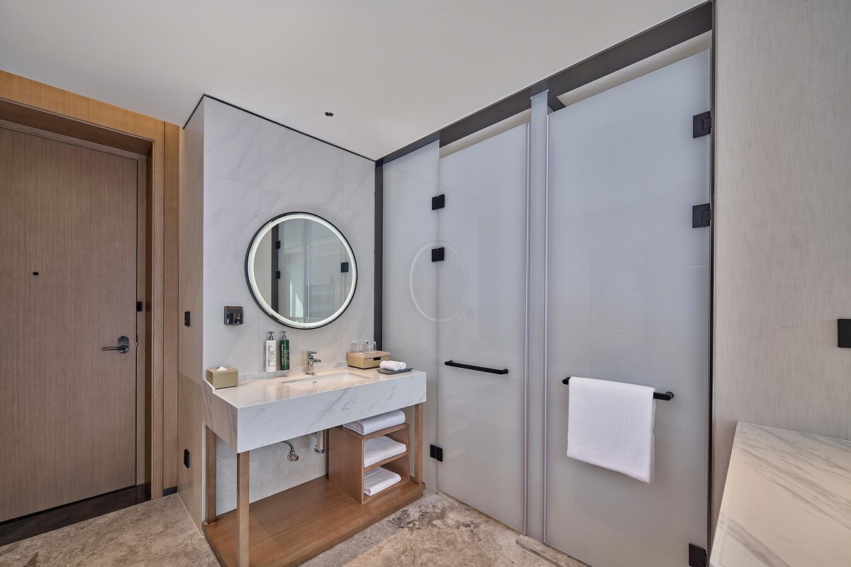 Ein modernes Badezimmer mit Marmorwaschtisch, rundem Spiegel und barrierefreier Dusche.