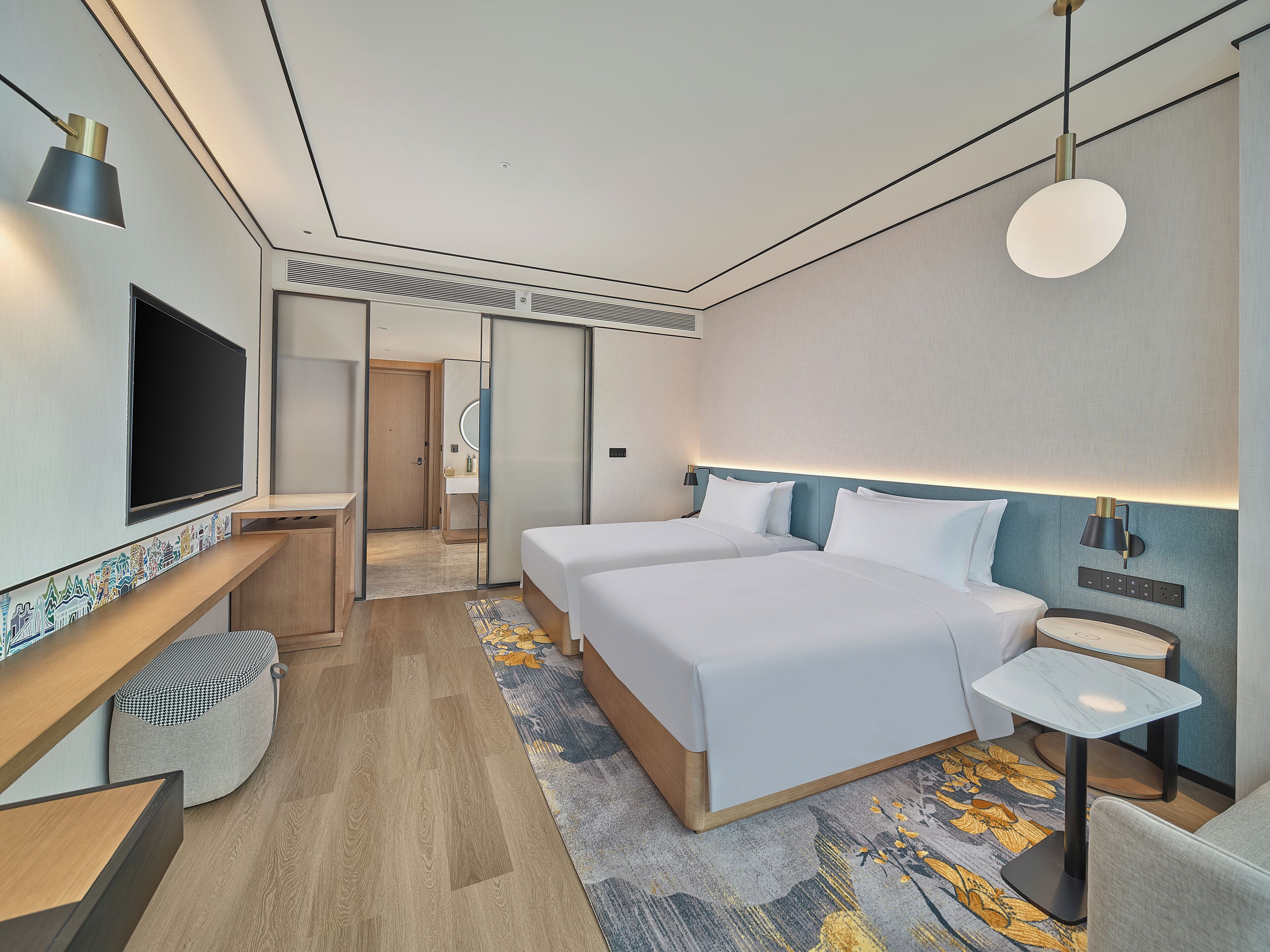 A modern hotel room with two beds, a TV, a desk, and a small table.