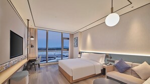 A modern hotel room with a large bed, a sofa, a dining table, and a TV. - Hilton Garden Inn Guangzhou Baiyun Airport Terminal 3 (Guangzhou)