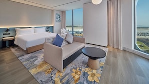 A modern hotel room with a large bed, a sofa, a small table, and a view of the airport. - Hilton Garden Inn Guangzhou Baiyun Airport Terminal 3 (Guangzhou)