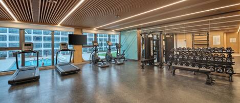 A modern gym with treadmills, elliptical machines, a squat rack, and a rack of dumbbells.