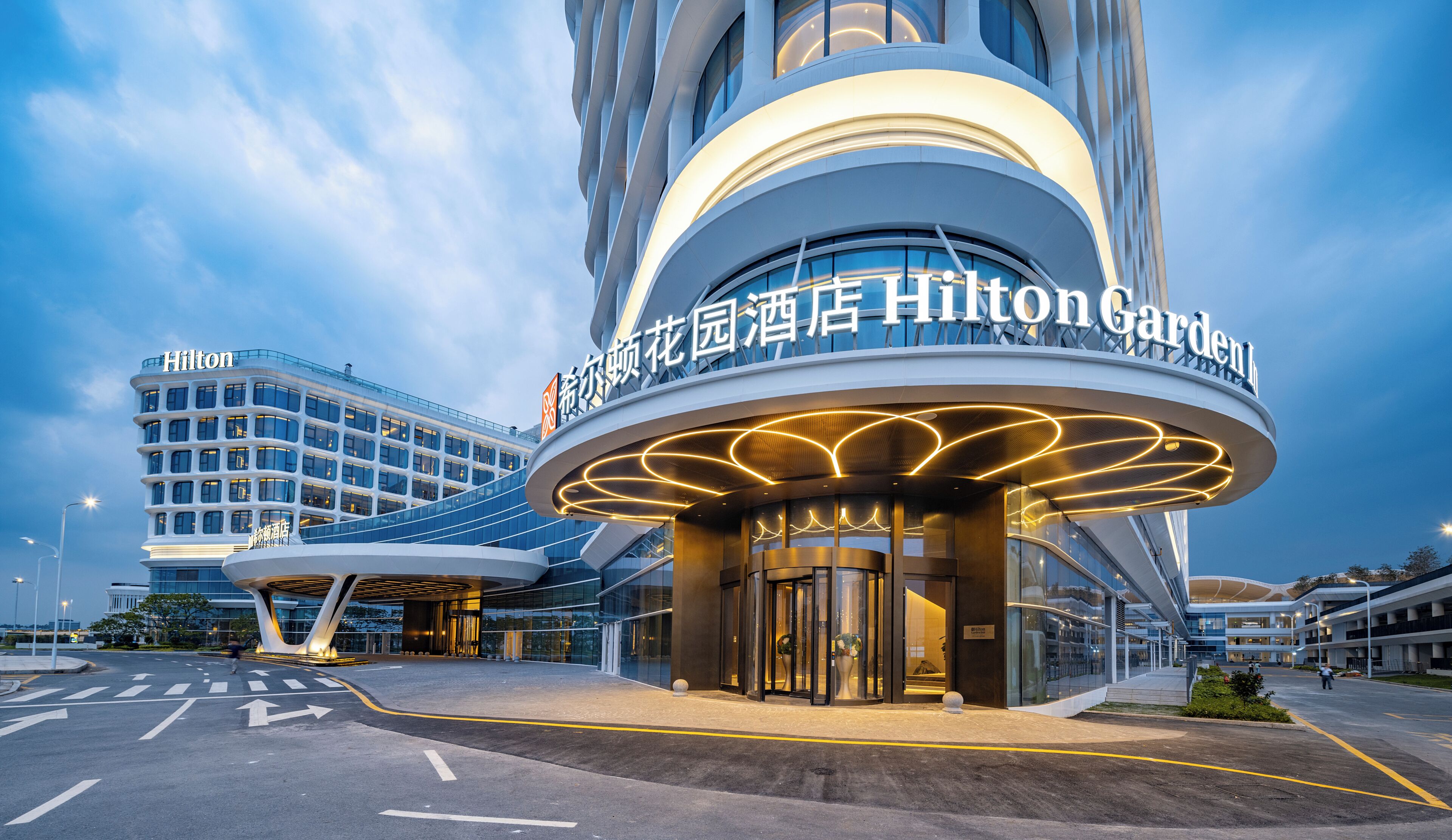 A modern hotel entrance with a curved facade and illuminated signage.