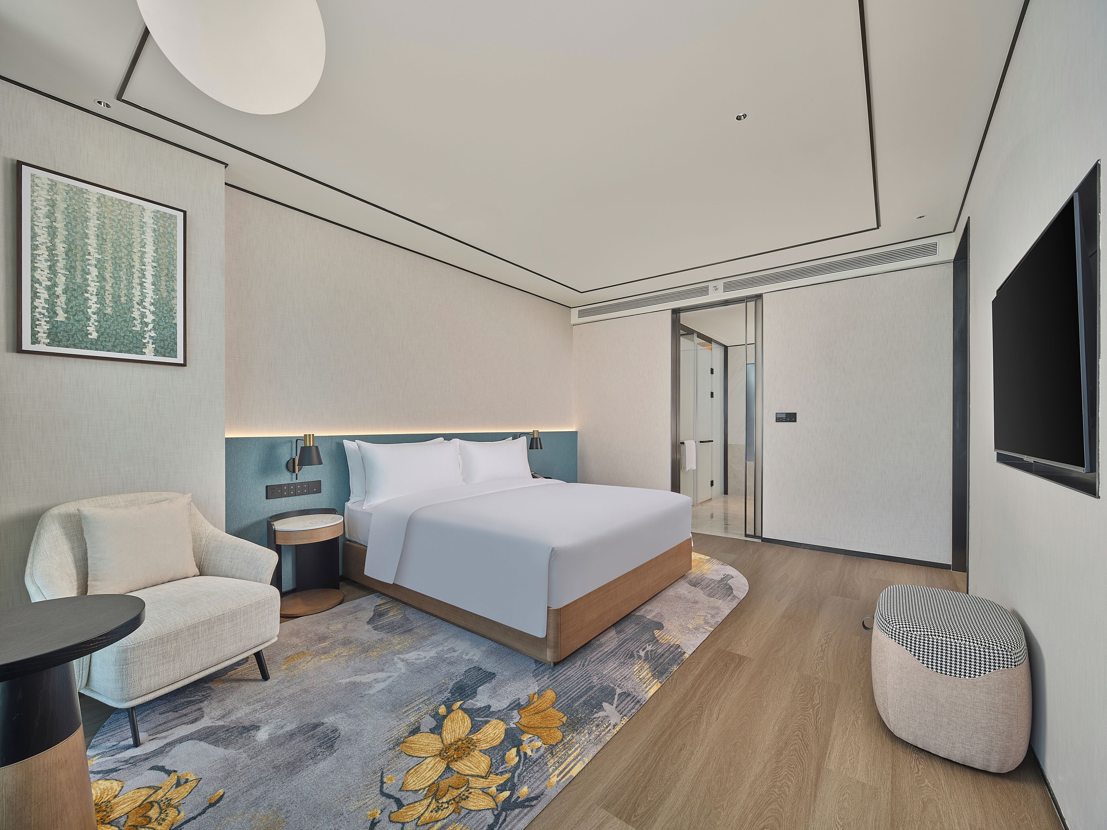 A modern hotel room with a bed, a chair, a bedside table, and a large window.