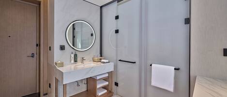 Un baño moderno con un lavamanos de mármol, un espejo redondo y una mampara de cristal.