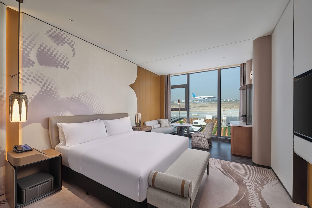 A modern hotel room with a large bed, a desk, a chair, and a TV.