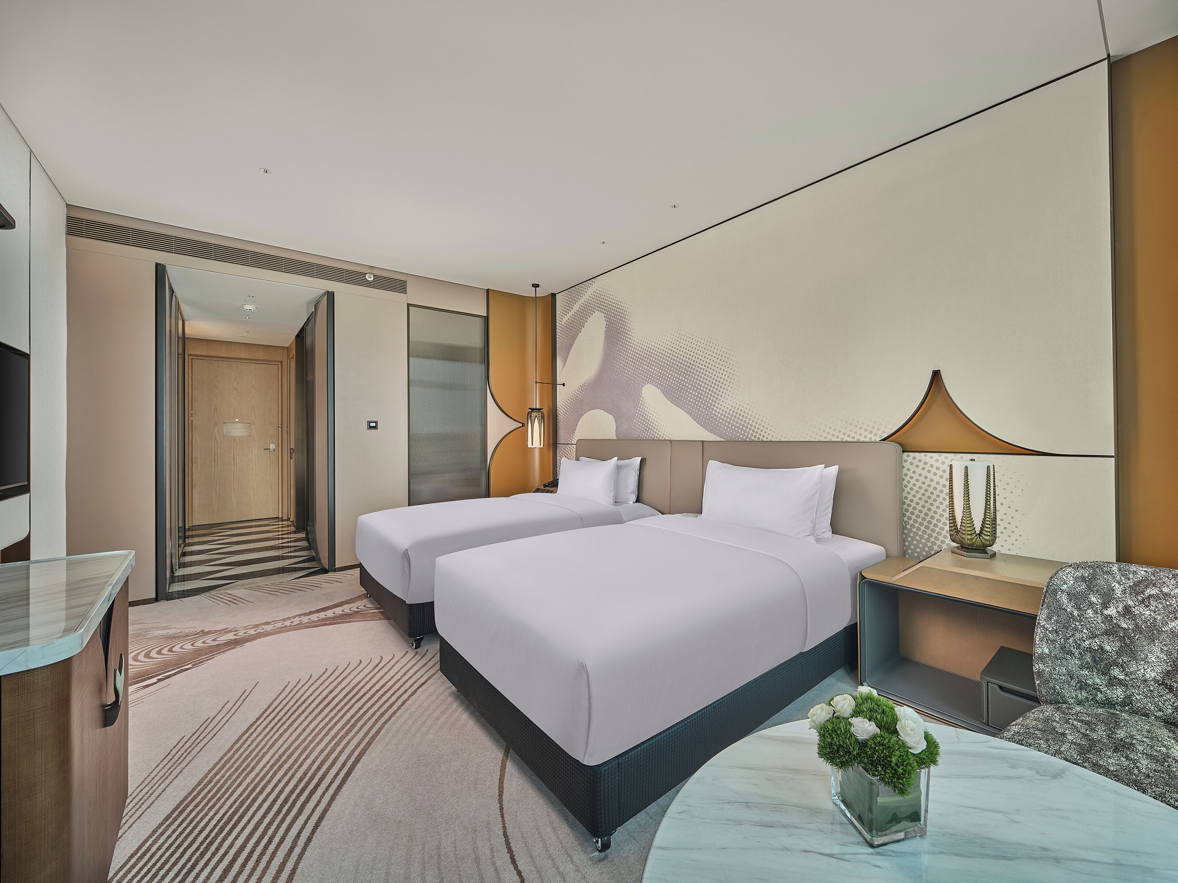 A modern hotel room with two beds, a sitting area, a TV, and a large window.