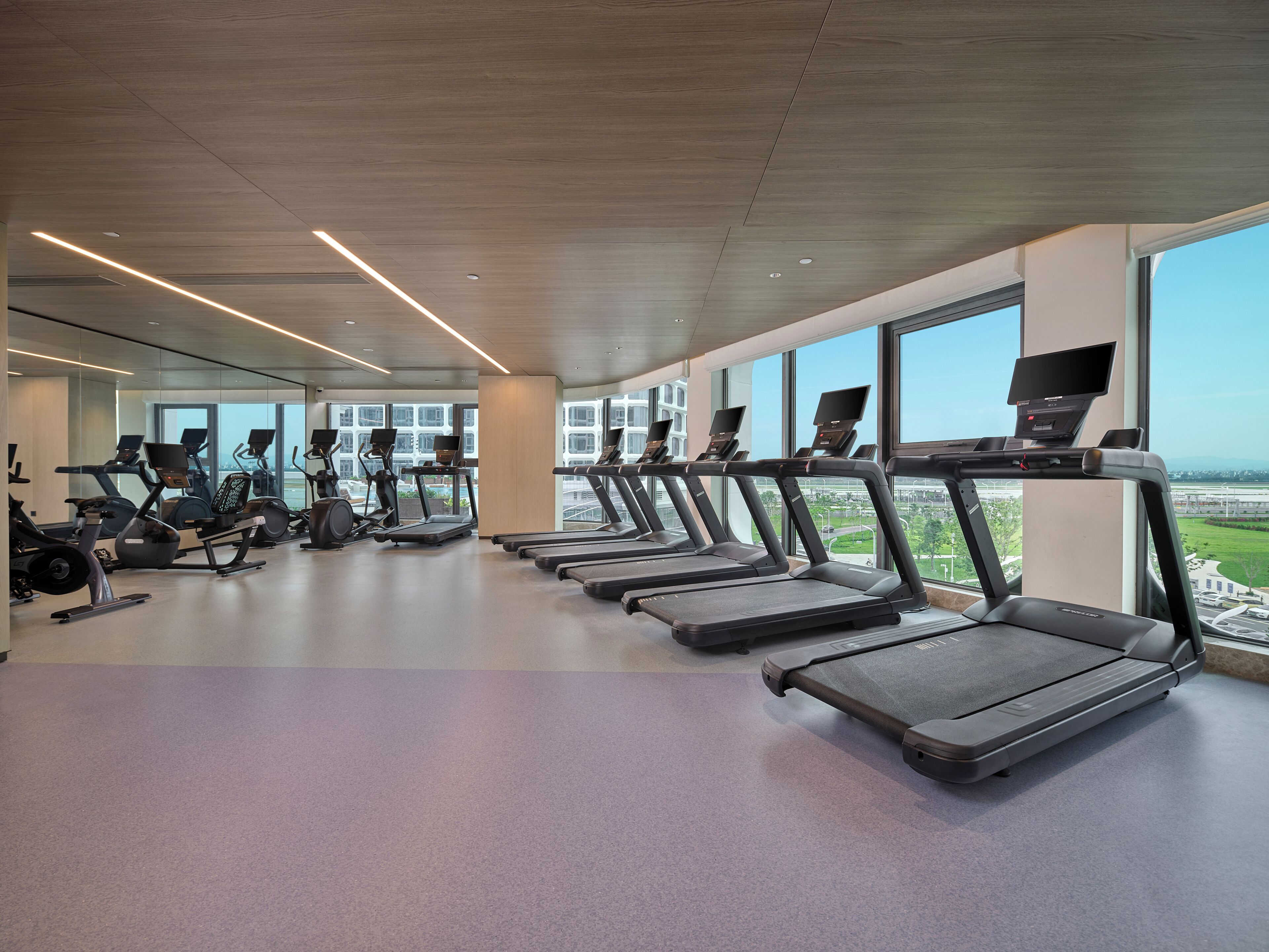 A gym with treadmills, exercise bikes, and a large window offering a view of the city.