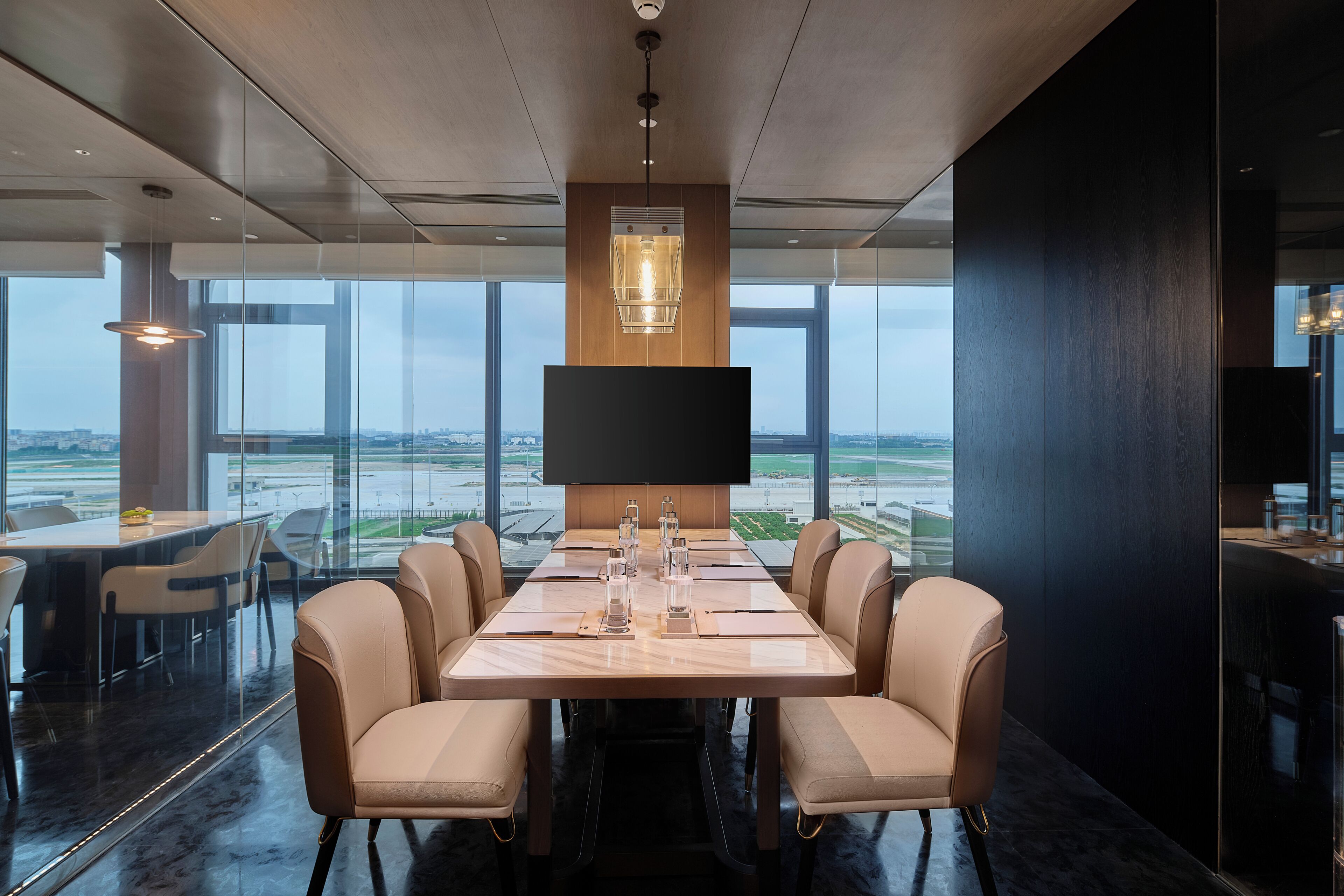 A modern conference room with a large table, comfortable chairs, a large screen, and a view of the airport.