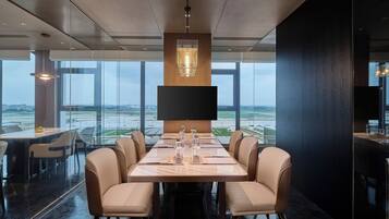 A modern conference room with a large table, comfortable chairs, a large screen, and a view of the airport.