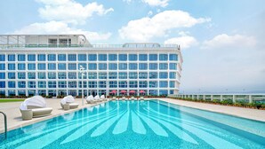 A modern hotel with a large pool, outdoor seating, and a view of the ocean. - Hilton Guangzhou Baiyun Airport Terminal 3 (Guangzhou)
