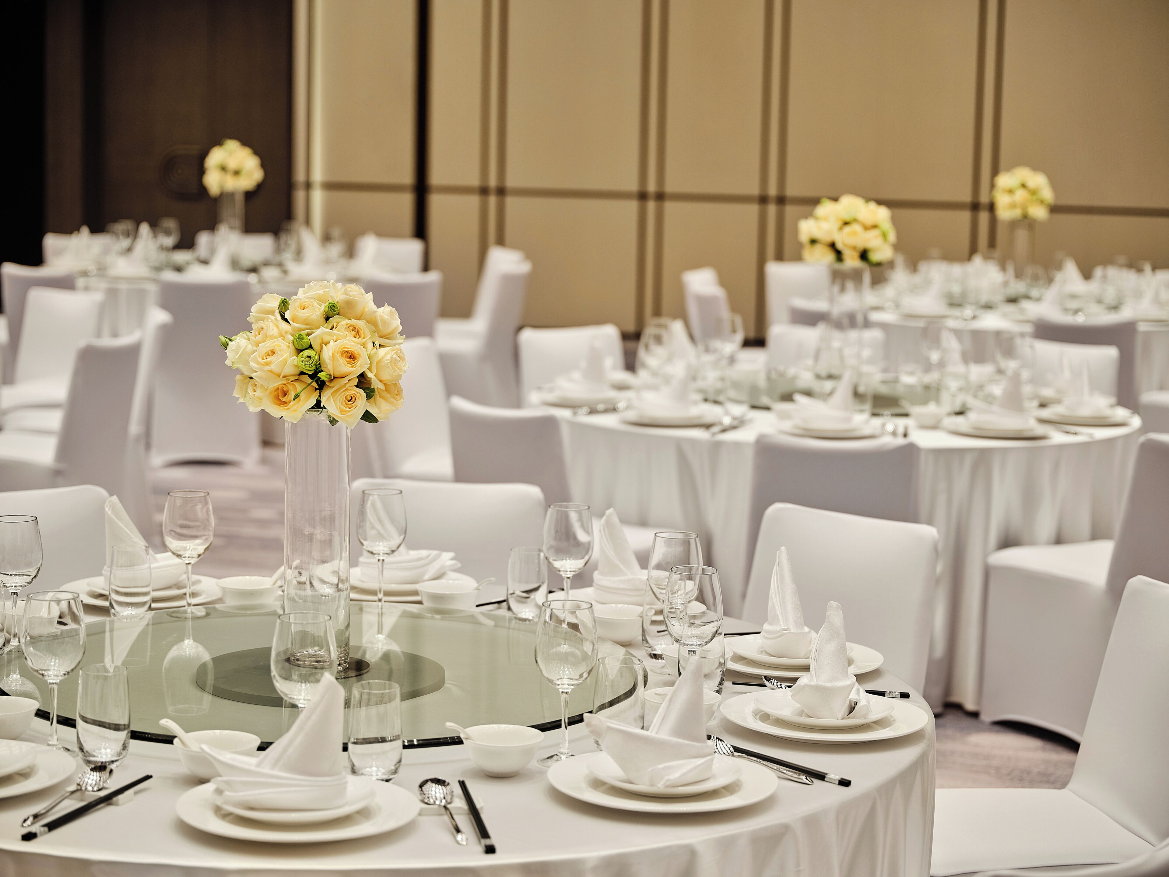 A banquet hall with round tables, white chairs, and floral centerpieces.