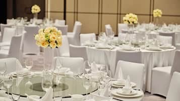 A banquet hall with round tables, white chairs, and floral centerpieces.