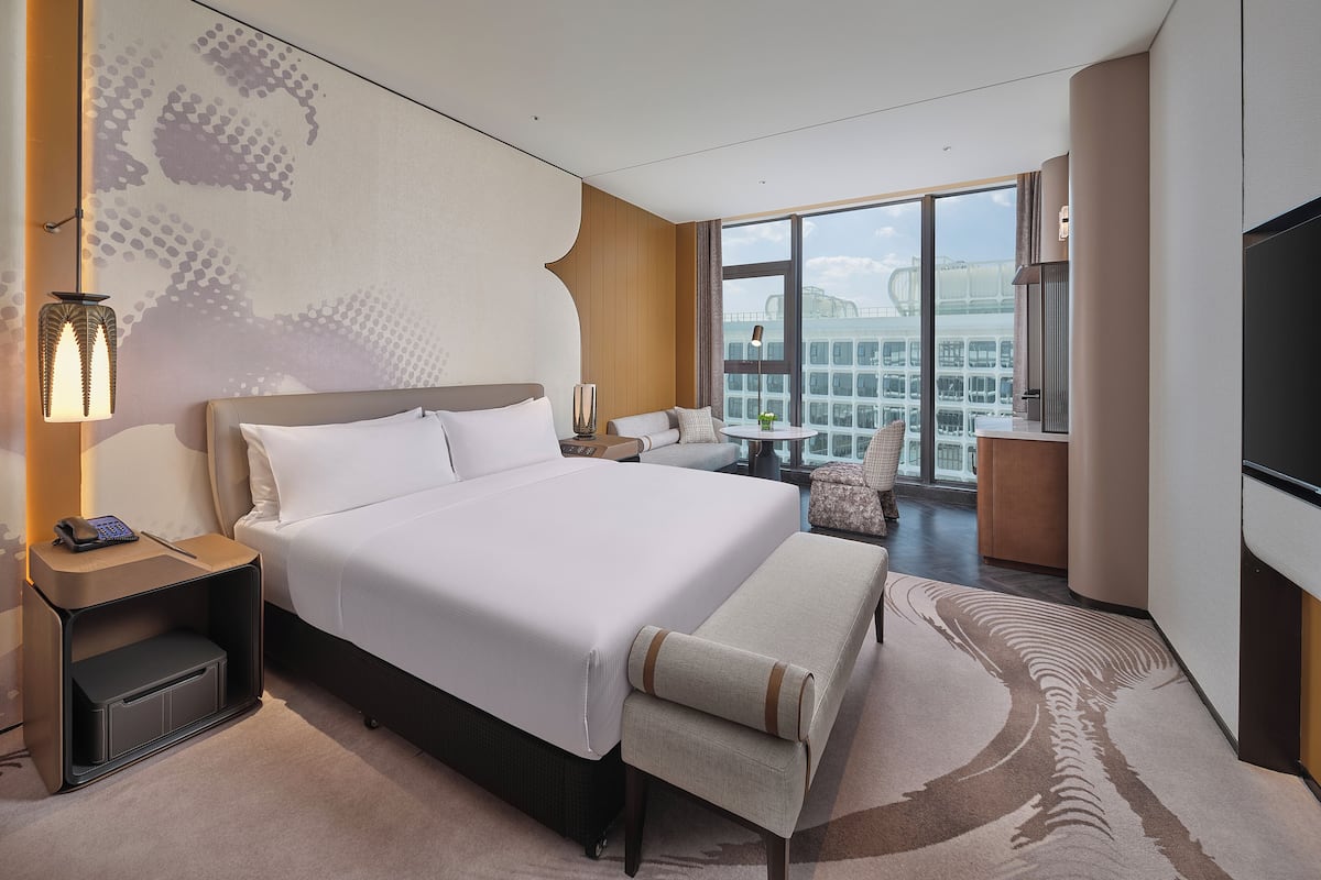 A hotel room with a large bed, a desk, a chair, a small table, and a TV.
