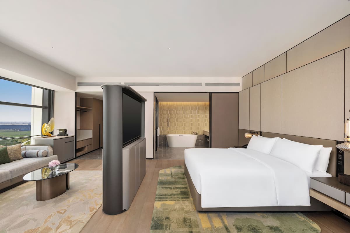 Ein modernes Hotelzimmer mit einem großen Bett, einem Flachbildfernseher, einer Couch, einem Couchtisch und Blick auf die Stadt.