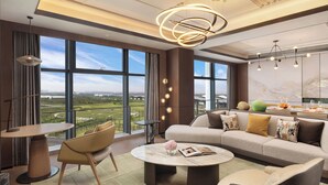 A modern living room with a sofa, coffee table, and chairs, large windows with a view of the city, and a unique ceiling light fixture. - Doubletree By Hilton Zhengzhou Airport Aerotropolis (Zhengzhou)
