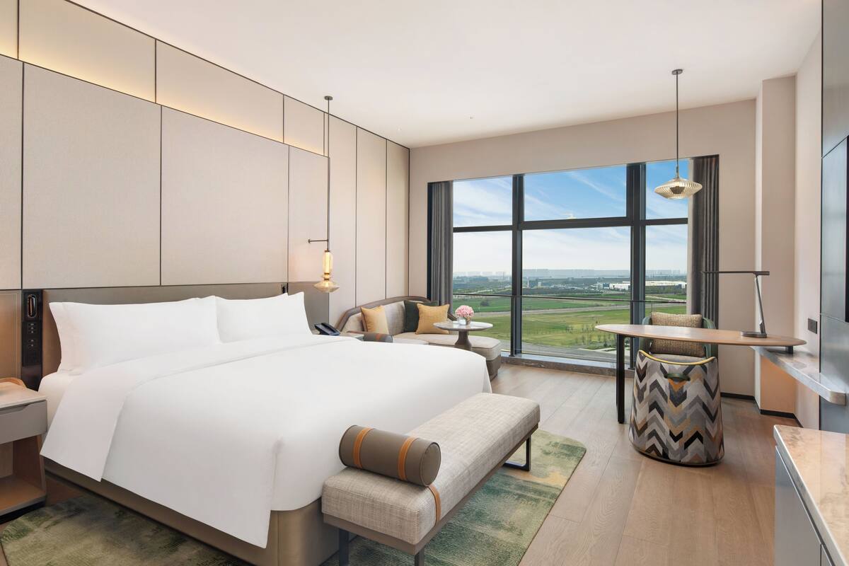 Ein modernes Hotelzimmer mit einem großen Bett, einer Sitzecke, einem Esstisch und Blick auf die Stadt.