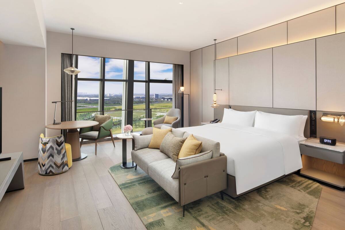Ein Hotelzimmer mit einem großen Bett, einer Couch, einem Esstisch und Blick auf die Stadt.