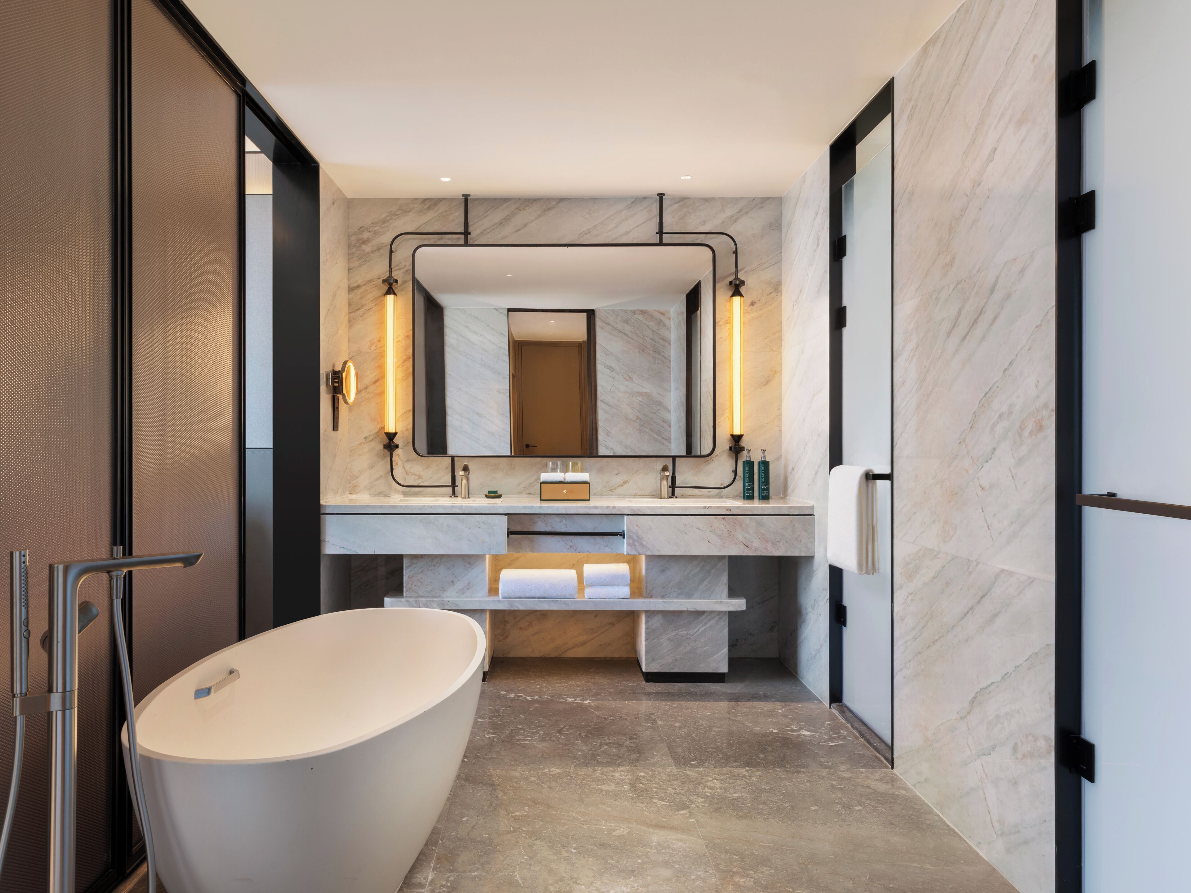 Un baño moderno con una bañera independiente, un espejo grande y un tocador con encimera de mármol.