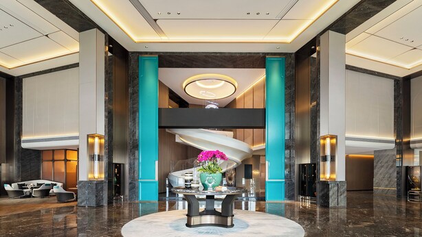 A modern lobby with a central spiral staircase, a round table with a vase of flowers, and a seating area with sofas and chairs. - Doubletree By Hilton Zhengzhou Airport Aerotropolis (Zhengzhou)