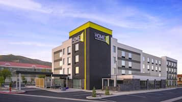 Un hotel moderno con un llamativo letrero 'HOME2', un estacionamiento y montañas al fondo.