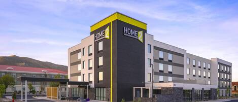 A modern hotel with a prominent 'HOME2' sign, a parking lot, and a mountain backdrop.
