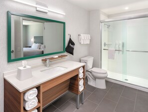 Un baño moderno con un espejo grande, un lavabo con tocador de madera, un inodoro y una ducha con mampara de vidrio.
