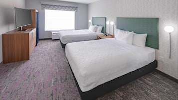 A hotel room with two beds, a TV, a desk, and a window with a view.