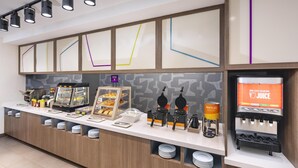 Una barra de desayuno con máquinas para hacer gofres, dispensador de zumo y cafetera.