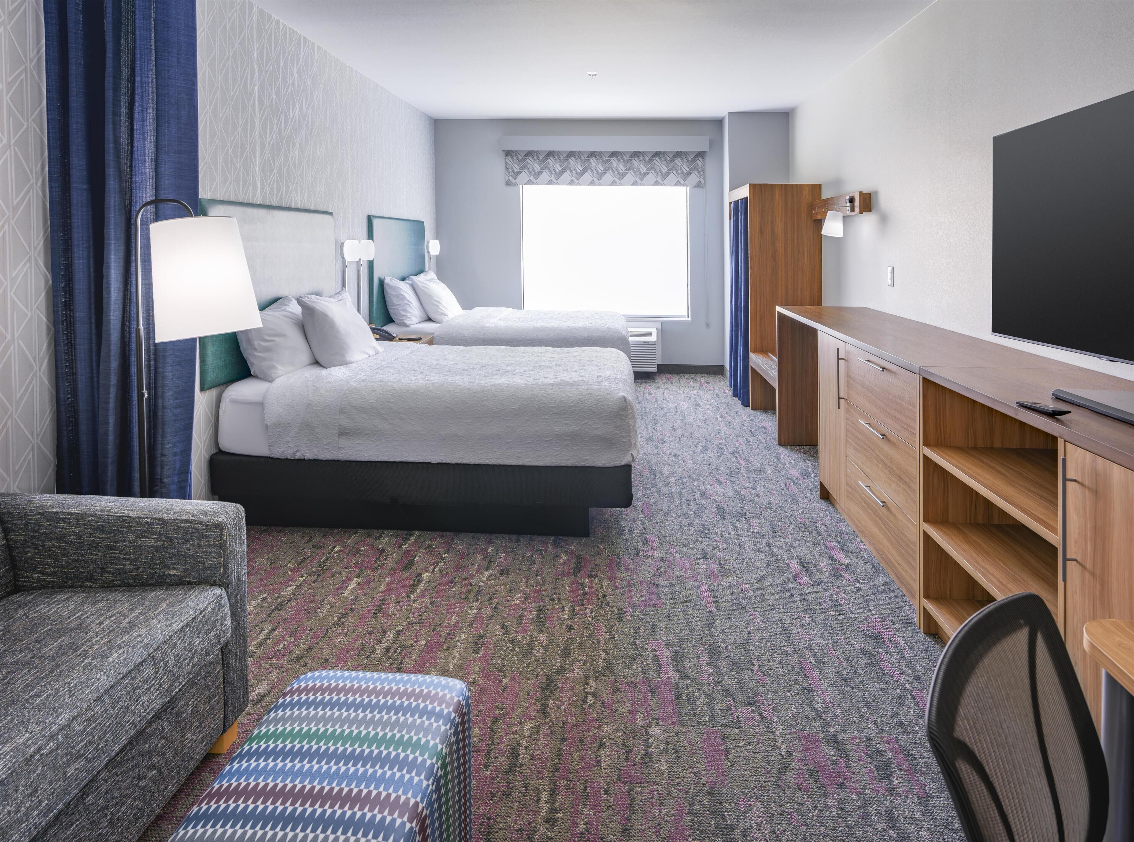 Quarto de hotel com duas camas, uma mesa, uma cadeira e uma televisão.