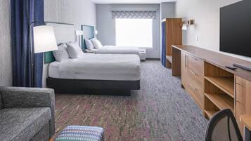 Quarto de hotel com duas camas, uma mesa, uma cadeira e uma televisão.