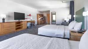 Habitación de hotel con dos camas, televisión, escritorio, kitchenette y baño.