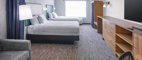 A hotel room with two beds, a desk, a chair, and a television.