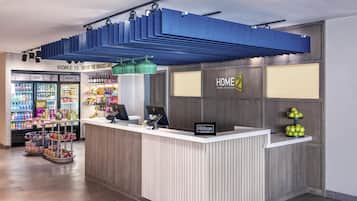 Un espace d’accueil d’hôtel comprenant un comptoir, des distributeurs automatiques et un panneau indiquant « Home 2 Suites by Hilton ».