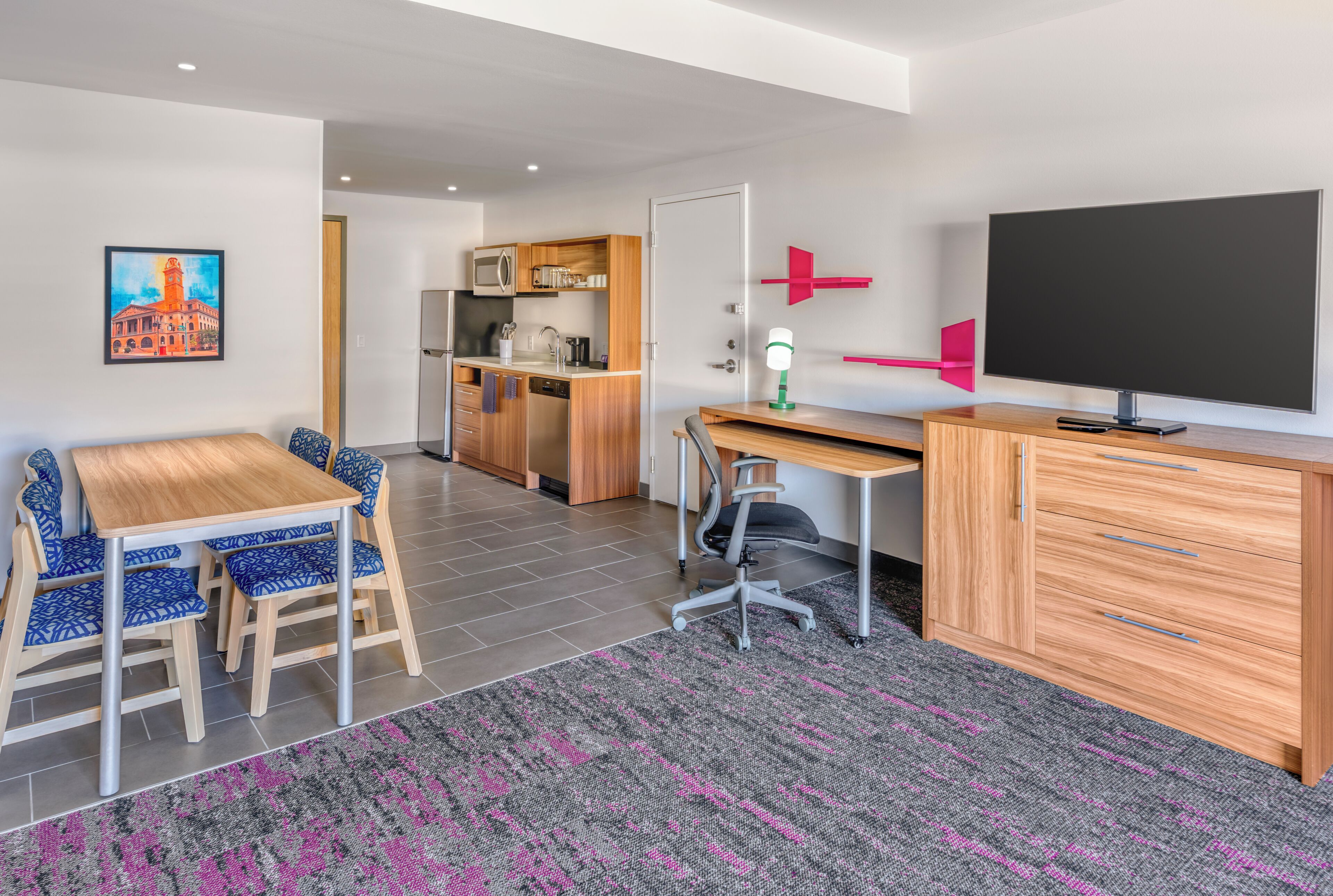 Een moderne kamer met een eettafel, stoelen, een bureau, een televisie en een kitchenette.