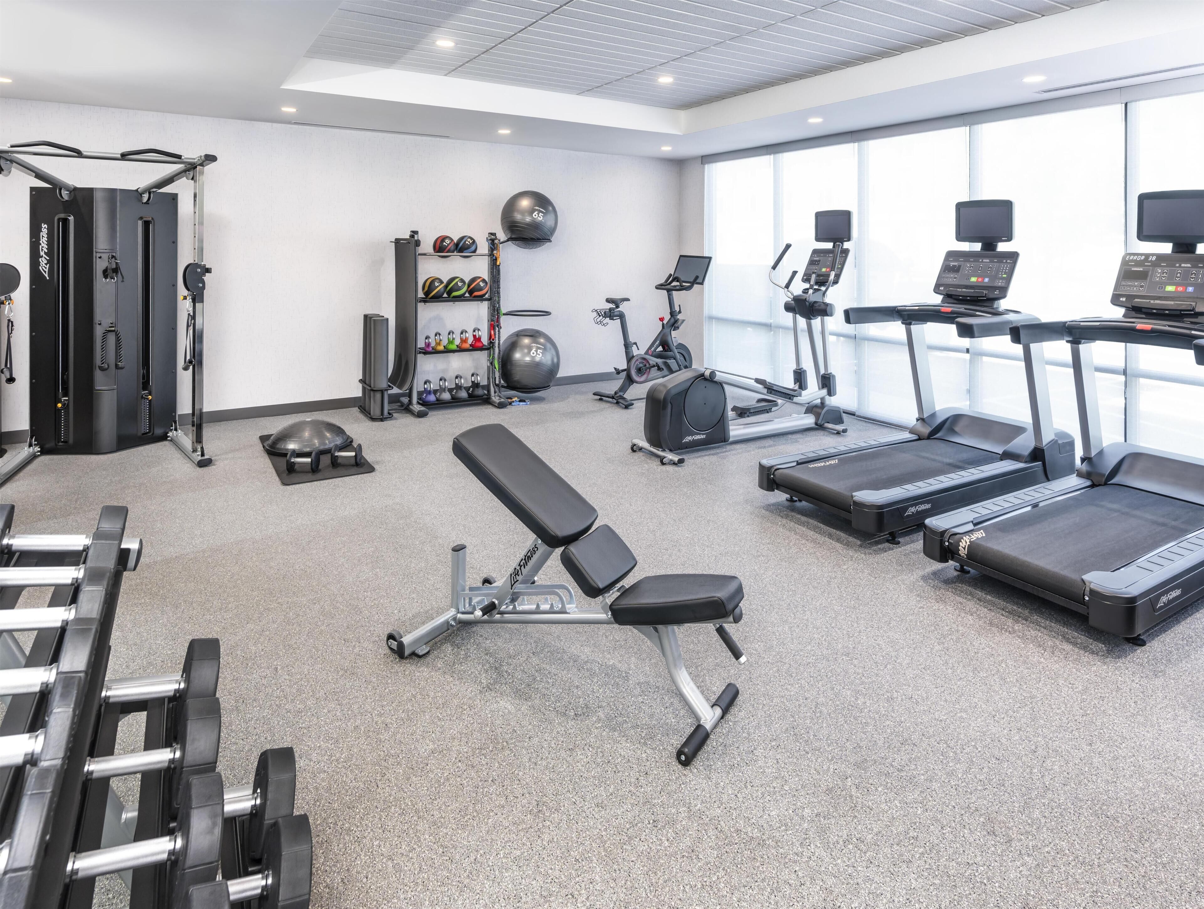 Ett gym med löpband, en bänk, hantlar och träningsbollar.