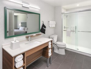 A modern bathroom with a large mirror, a wooden vanity, a toilet, and a glass-enclosed shower. - Home2 Suites By Hilton Carson City (Carson City)