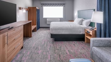 A hotel room with a bed, bedside table, lamp, TV, dresser, and a window with curtains.