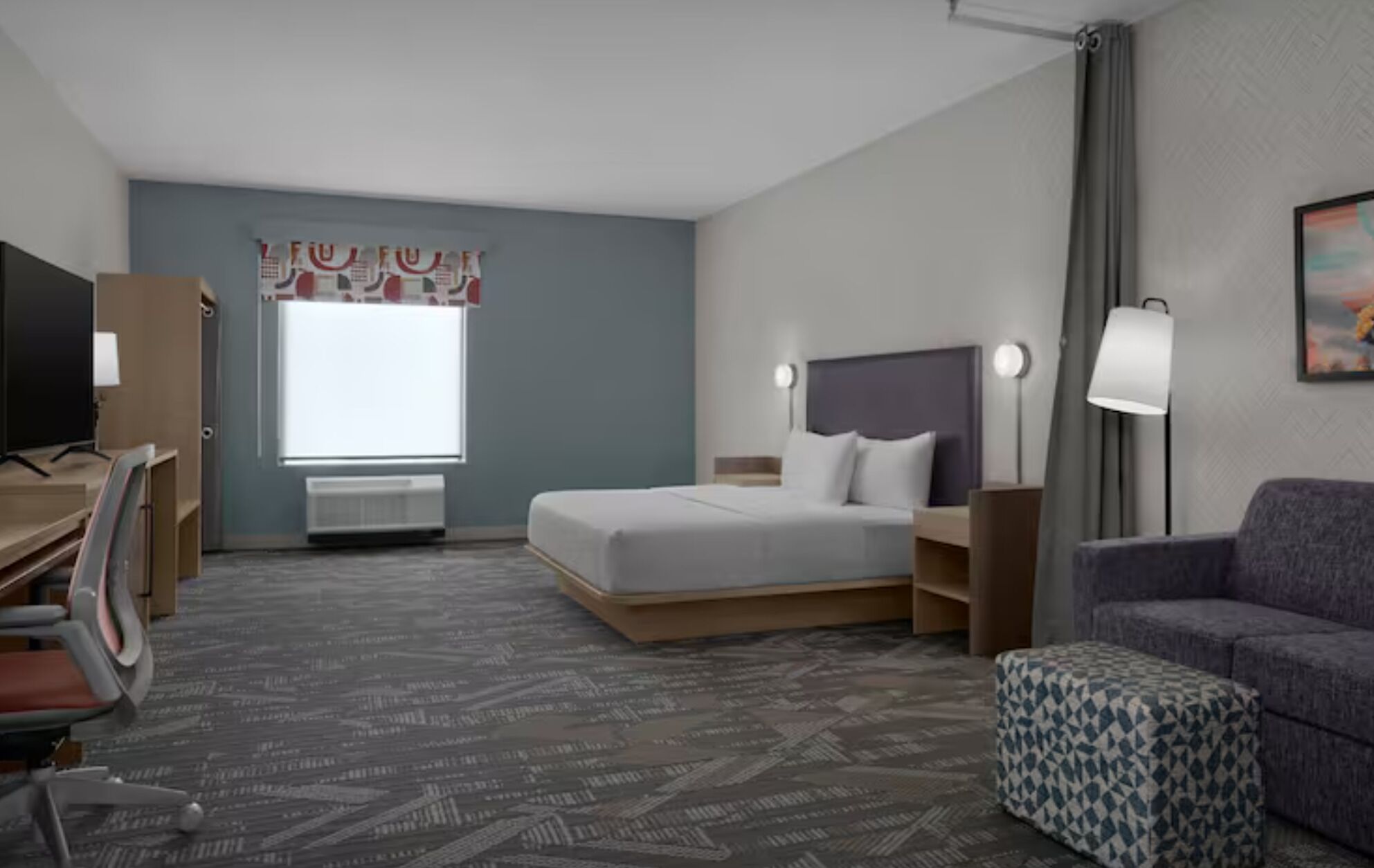 A hotel room with a bed, a desk, a chair, a couch, and a window with curtains.