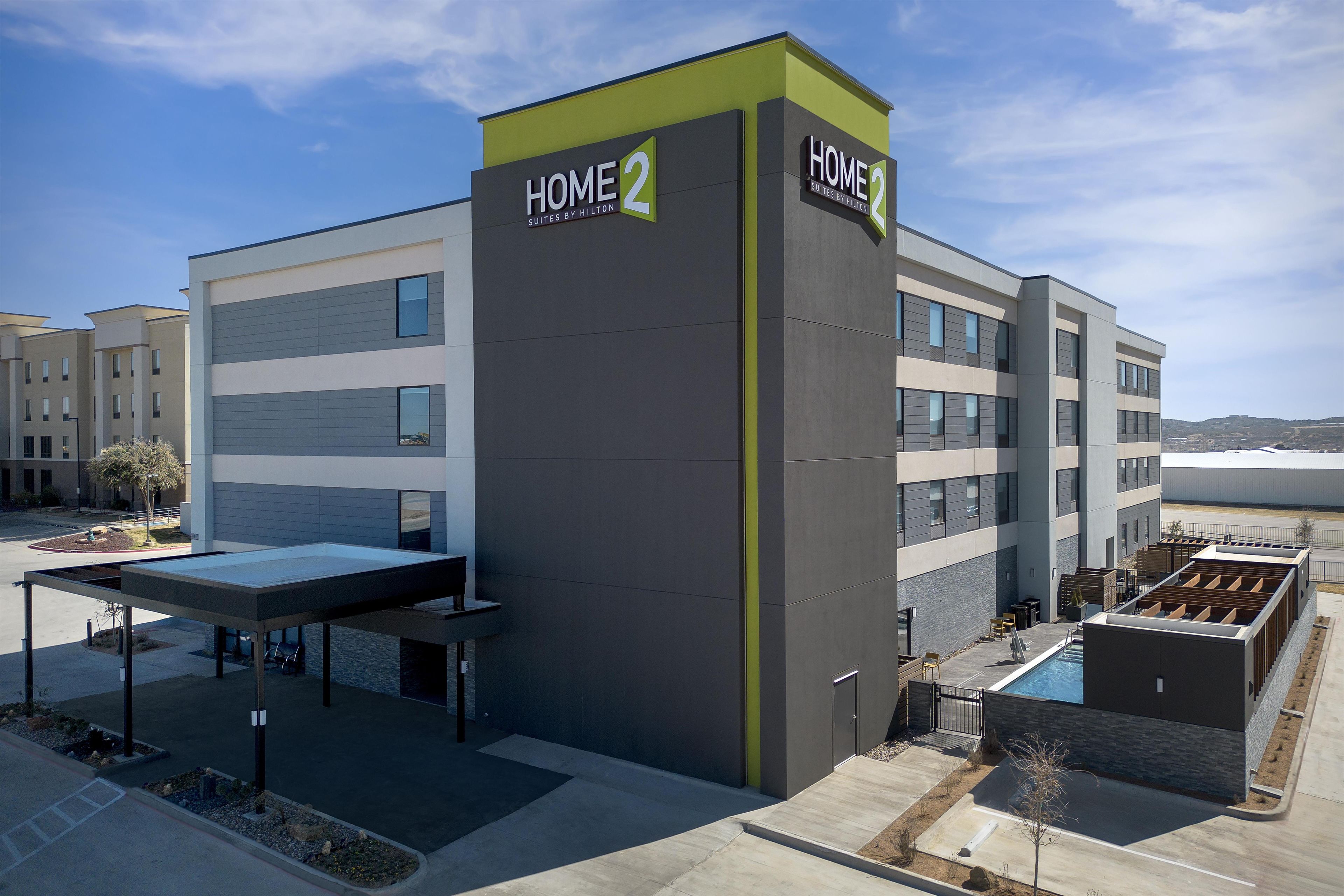 A modern hotel building with a sign reading 'HOME 2 Suites by Hilton.'