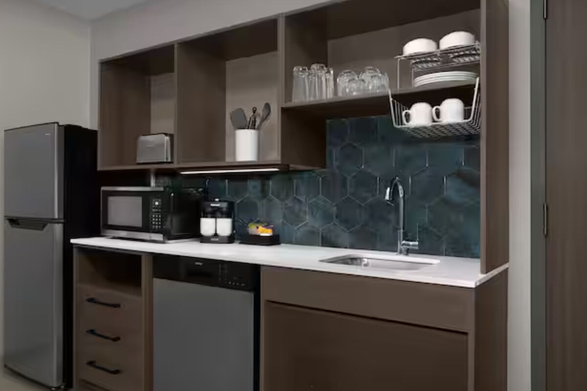 A modern kitchen with a refrigerator, microwave, coffee maker, and a sink.
