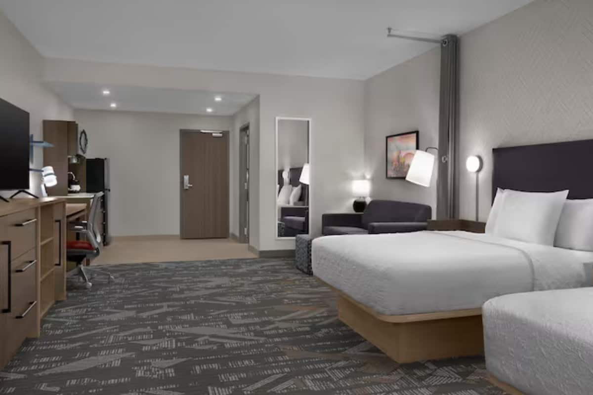Una habitación de hotel con cama, escritorio con ordenador, cómoda, espejo y puerta.