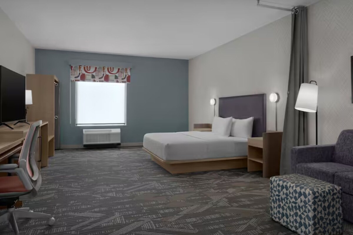 A hotel room with a bed, a desk, a chair, a couch, and a window with curtains.