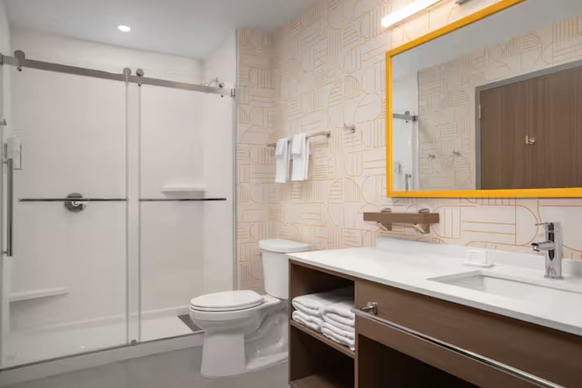 A modern bathroom with a glass shower enclosure, a toilet, a sink with a mirror, and a towel rack.