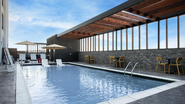An indoor swimming pool with a stone wall, wooden ceiling beams, and yellow chairs.