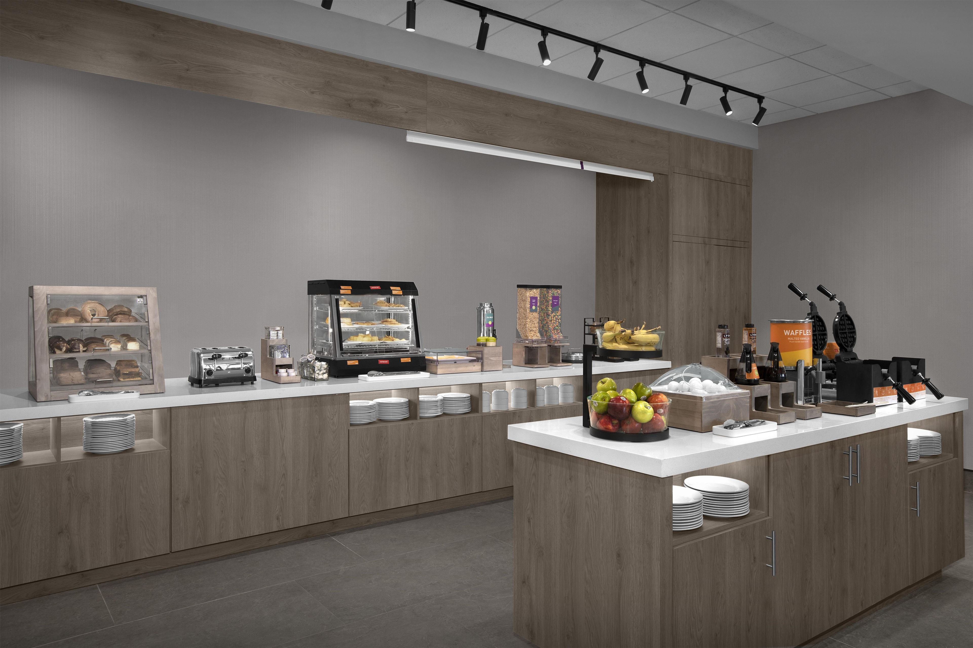A modern breakfast bar with a toaster, a glass display case with pastries, and a fruit bowl.