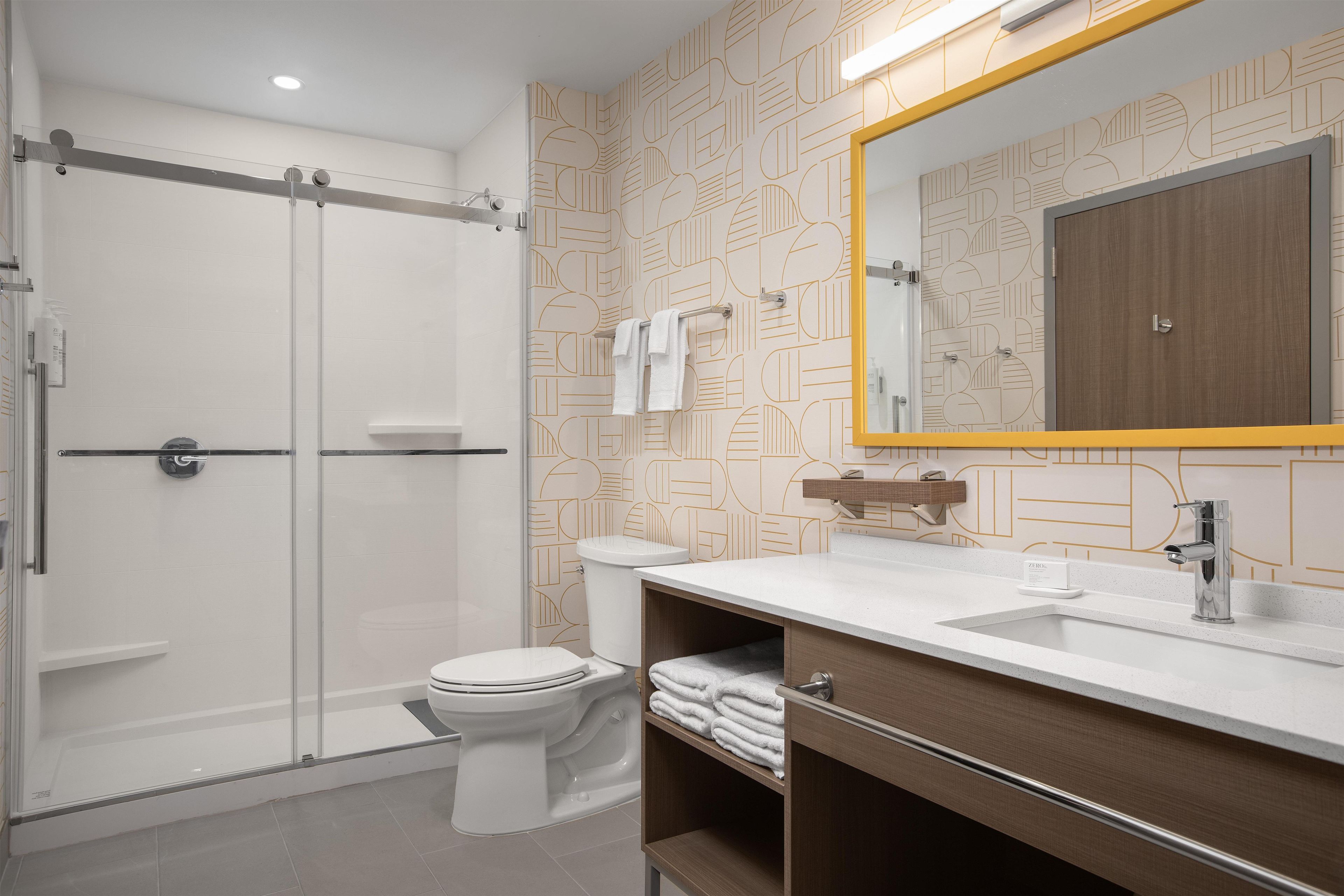 A modern bathroom with a walk-in shower, toilet, and vanity with a mirror.