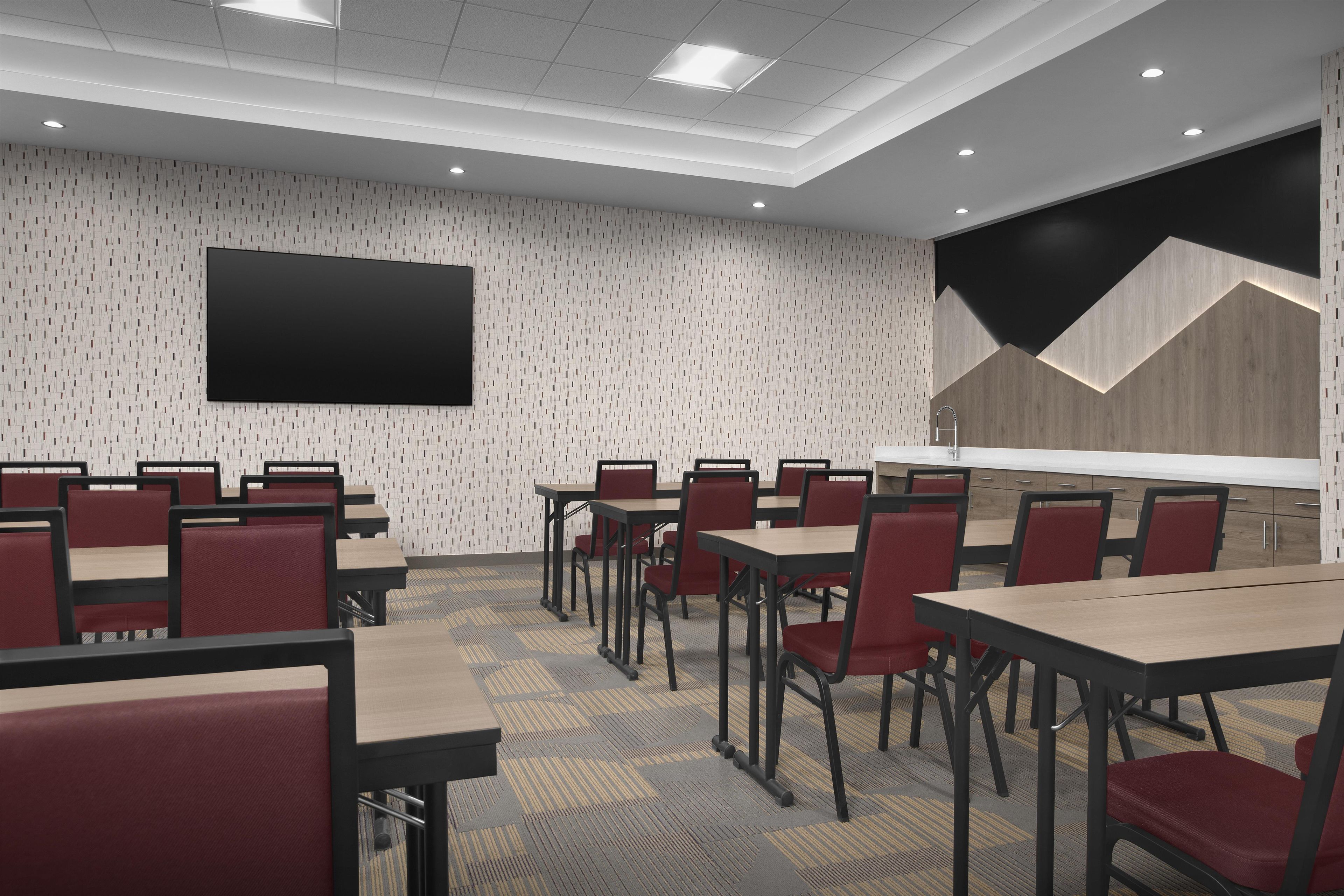 A conference room with a large flat-screen TV, multiple tables and chairs, and a patterned wall.