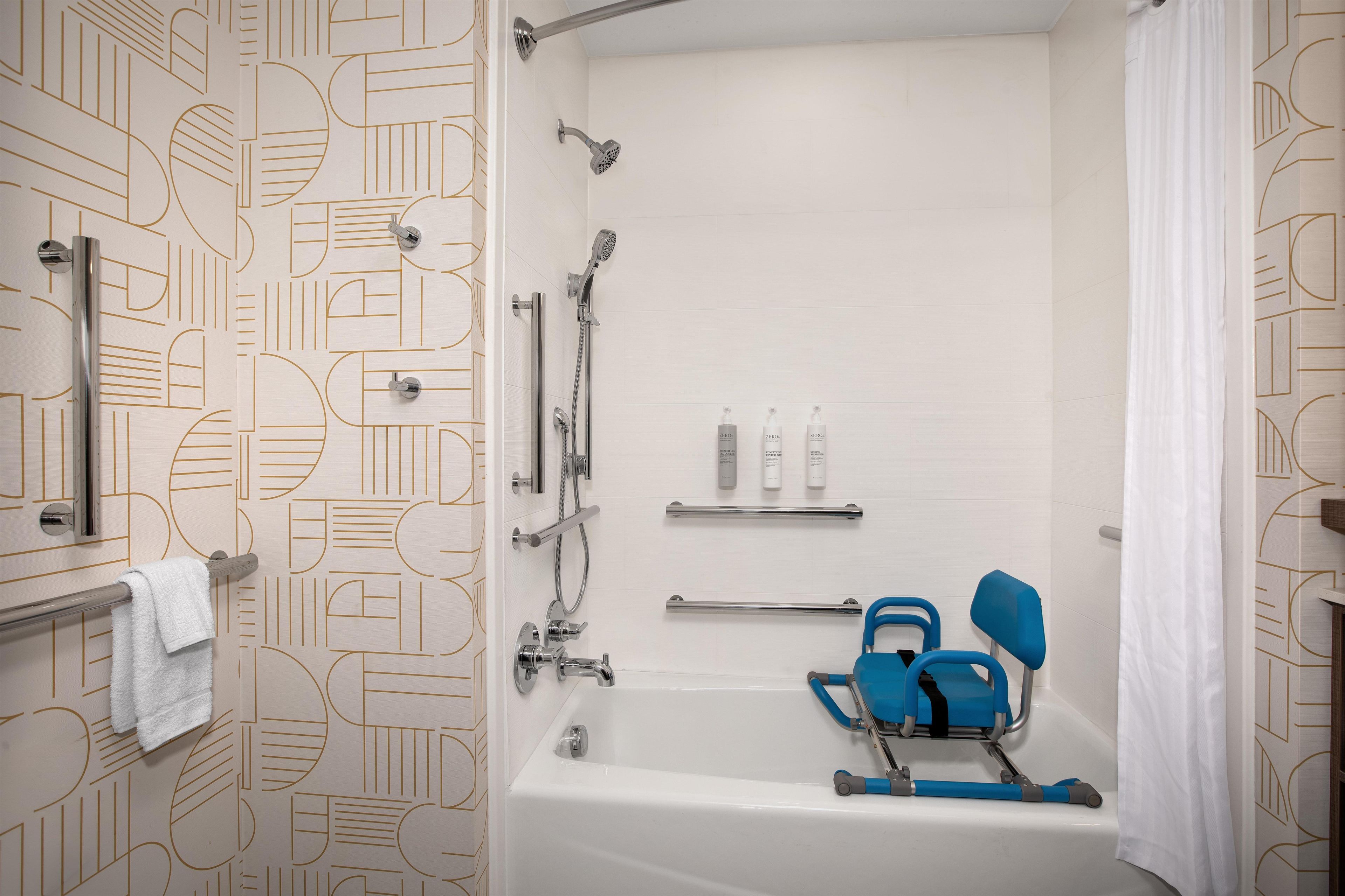 A modern bathroom with a bathtub, shower, and grab bars. There are toiletries on a shelf and a towel rack.