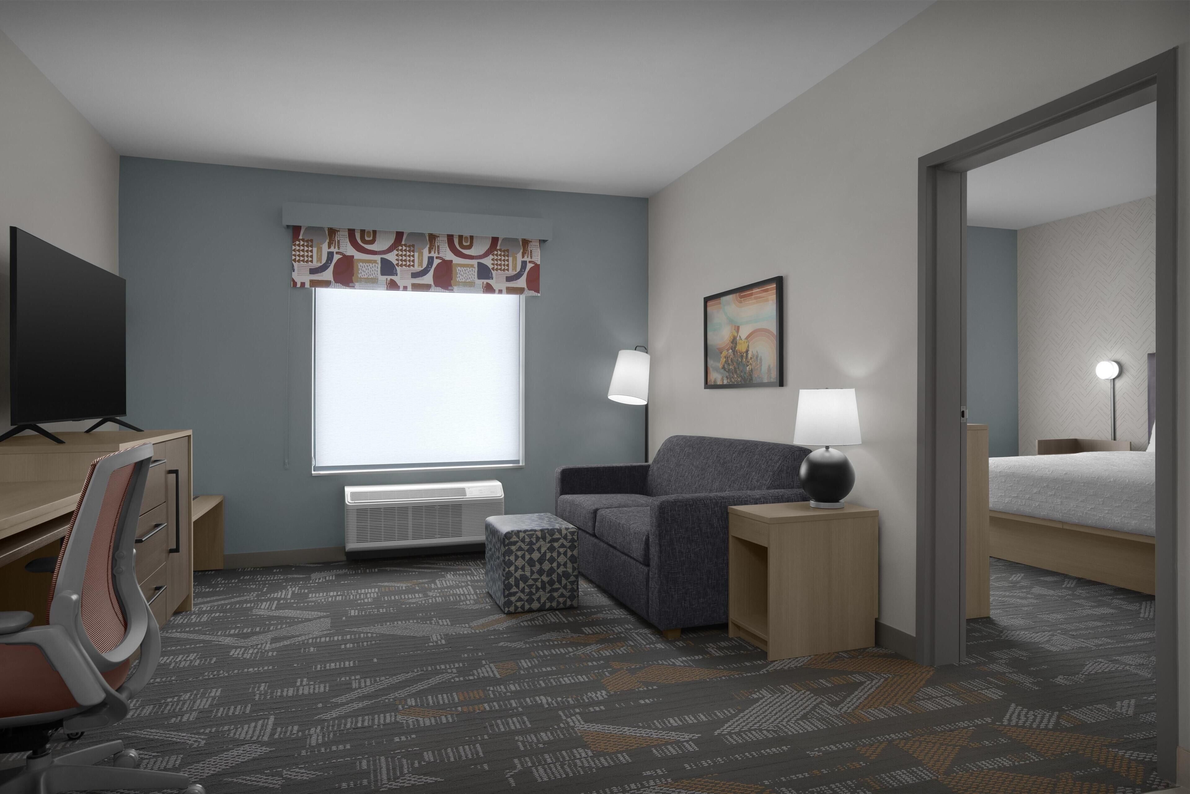 Una habitación de hotel con escritorio, silla, sofá, mesita de noche, lámpara y cama.